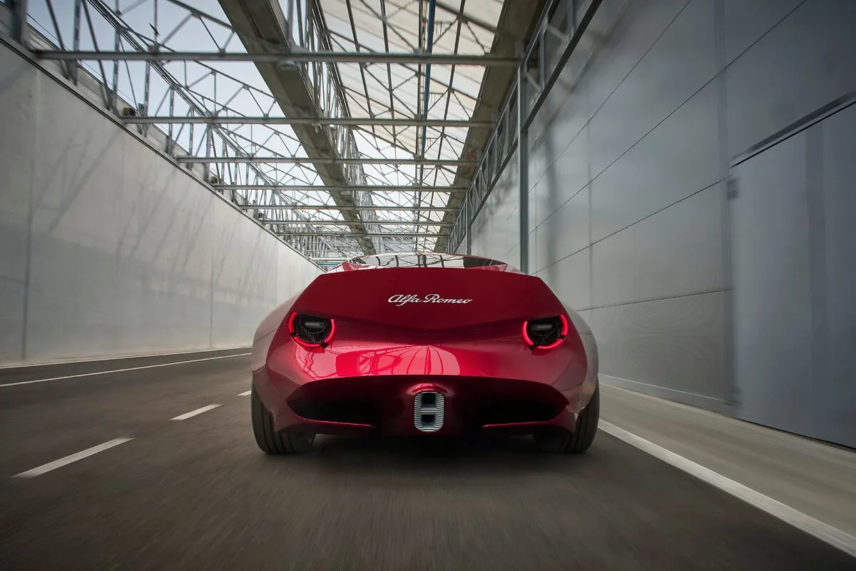 Rode Alfa Romeo Cuorerosso rijdend van achteren gezien, met ronde achterlichten en afgeknotte achterkant