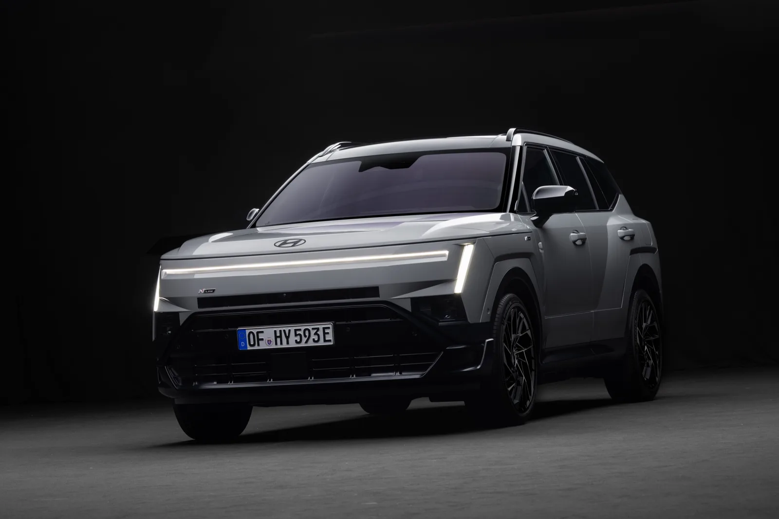 Grijze Hyundai Tucson N Line van schuin voren in een donkere studio, met verlichte lichtbalk
