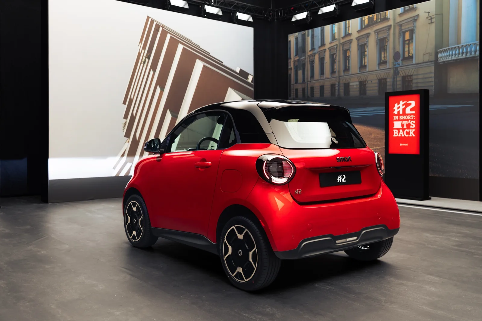 Rode smart #2 van schuin achteren op een beursstand, met tweekleurige carrosserie en achterklep in twee delen